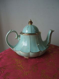 a tea pot sitting on top of a table next to a pink table cloth with gold trim