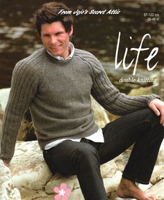 a man is sitting on some rocks by the water wearing a sweater and black pants