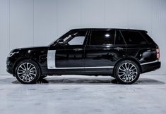 a black and white range rover parked in front of a gray wall with chrome rims