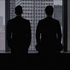 two men standing in front of a large window looking out at the city below them