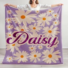 a woman holding up a purple and white daisy blanket with the word daisy printed on it