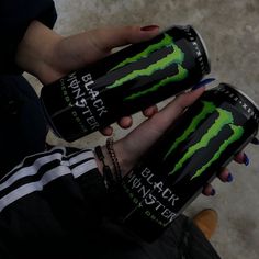 a woman holding two cans of monster energy drink in one hand and another person's hand on the other