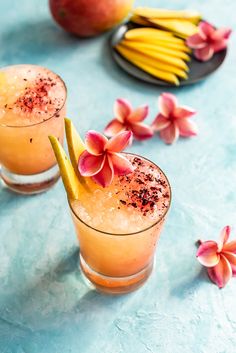 two glasses filled with orange juice and garnished with flowers on a blue surface