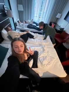 two people laying in bed with one pointing at the camera while another person stands near them