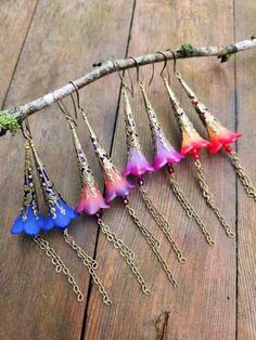 five different colored flowers are hanging from a branch on a wooden surface with chains attached to them