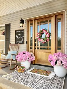 two large white vases filled with pink flowers sit on the front porch of a house