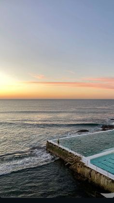 an empty swimming pool in front of the ocean with people standing on it at sunset