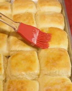 a red spatula is being used to brush down the top of some bread rolls