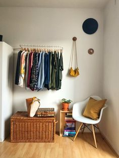 a room with clothes hanging on the wall and a chair in front of it next to a book shelf