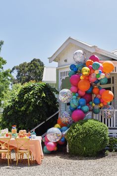 an outdoor party with balloons and decorations on the table, in front of a house