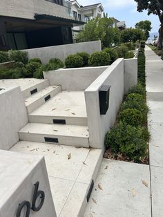 concrete steps lead up to the front door of a modern home with landscaping around them