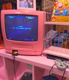 a pink computer monitor sitting on top of a desk next to a video game controller