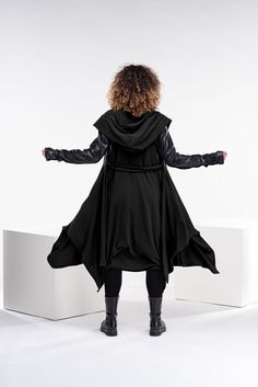 "This asymmetrical and modern cloak with a hood has two side pockets, a super comfy hood, and thumbholes for a fabulous look. Faux leather elements on the sleeves and the back and long belt as closure. The model in the picture is 176cm. ⅼ 5.8 ft. tall and is wearing size S / color: Black 🌟 INFO: * Worldwide EXPRESS shipping - please provide a phone number for shipping documents * US Sizing XS to 4XL - size chart available below - all measurements of the body * We offer customization to Personal Hooded Cape For Fall Cosplay, Hooded Winter Cape For Cosplay, Winter Hooded Cape For Cosplay, Hooded Cape For Cosplay In Winter, Fall Cape Outerwear For Cosplay, Winter Long Sleeve Cape For Cosplay, Witchy Long Sleeve Outerwear For Fall, Black Long Sleeve Witchy Outerwear, Gothic Cape Outerwear For Winter