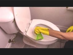 a person in yellow gloves cleaning a white toilet with a green rag on the seat