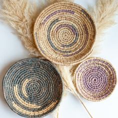 three woven baskets sitting on top of a white table next to some dry grass and feathers