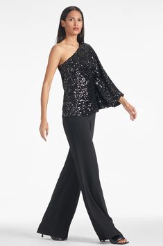 a woman wearing black pants and a one shoulder top with sequins on it