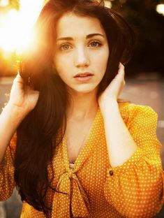 a woman with long dark hair wearing a yellow shirt and holding her hands to her head