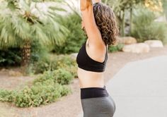 a woman in black top and grey leggings holding up her hand to the sky