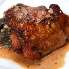 a piece of meat covered in sauce and spinach on top of a white plate