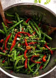 green beans and red peppers in a silver bowl with a wooden spoon on the side