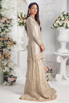 An elegantly embroidered shirt featuring gorgeous dabka work floral embroidery in gold & silver with sequins, pearls, resham, tila and gota work on stunning Maysuri net base. This classic ivory gold shirt is paired with stylish pleated dhaka pants. A fully embellished pure Indian Silk tissue dupatta, trimmed with lace, gota & kiran dhanak adding an elegant flair to final look. Pair this outfit with our hand-made potli bag, a must have outfit for Nikkah, engagement and other celebratory occasions Designer Gold Tissue Silk Palazzo Set, Gold Tissue Silk Palazzo Set For Eid, Gold Tissue Silk Palazzo Set With Resham Embroidery, Gold Palazzo Set With Dabka Work In Tissue Silk, Elegant Beige Salwar Kameez For Reception, Eid Cream Palazzo Set With Mirror Work, Cream Palazzo Set With Mirror Work For Eid, Elegant Beige Palazzo Set For Diwali, Designer Party Wear Sharara With Intricate Embroidery