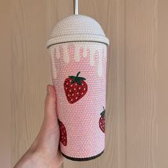 a hand holding a cup with strawberries on it and the lid covered in sequins