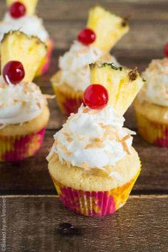 pineapple cupcakes with whipped cream and cherries on top, sitting on a wooden table