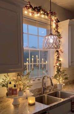 a kitchen sink under a window with christmas lights hanging from it's side and candles on the windowsill