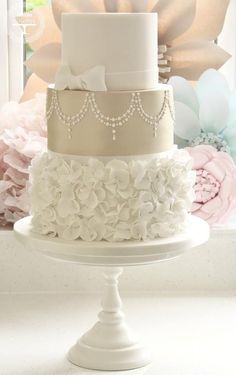 three tiered wedding cake with white flowers on the side and pink peonies in the background