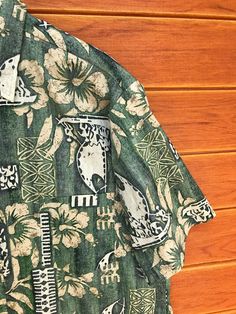 a green hawaiian shirt with white and black designs on the front, sitting against a wooden wall