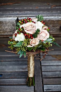 a bridal bouquet with roses, berries and greenery is sitting on a bench