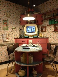 a table with chairs and a tv in the corner behind it on top of a shelf