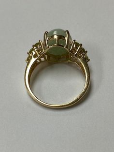 Lady's 14 karat yellow gold ring, with a large oval green jadeite jade at the center and accented by 12 round full cut natural peridot gemstones. The jade measures 14.0 mm x 10.0 mm with a depth of 4.65mm. The 12 round peridot measure approximately 2.5mm each. The ring is a size 8 and can be sized up or down. The ring weighs 4.72 grams. The ring is from an estate here in Hawai'i. The item is C11870/2 Please let me know if you have an questions. Mahalo for looking at my item. Green Multi-stone Oval Cabochon Jewelry, Oval Multi-stone Emerald Ring, Green Oval Cabochon Ring With Accent Stones, Green Oval Cabochon Ring With Center Stone, Oval Green Emerald Ring With Gemstone Accents, Oval Green Multi-stone Gemstones, Green Oval Multi-stone Gemstones, Green Oval Prehnite Rings, Green 14k Stamped Round Rings