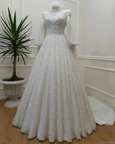 a white wedding dress on display in a room with a potted plant behind it