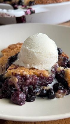 blueberry cobbler with ice cream on top in a white bowl sitting on a wooden table