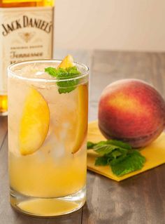 a glass filled with lemonade next to two peaches