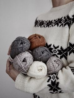 a woman is holding balls of yarn in her hands and wearing a sweater with an ornament pattern on it