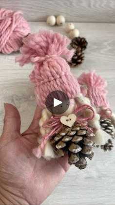 a hand holding a small pine cone with a knitted animal on it's head