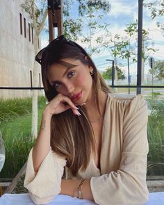 a beautiful young woman sitting at a table with her hand on her chin and looking into the camera