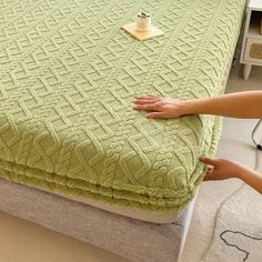 a woman is placing her hand on the edge of a green bedspread that has been made