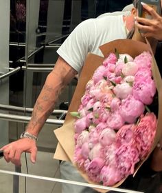 a man holding a bouquet of pink flowers in his hand and taking a selfie