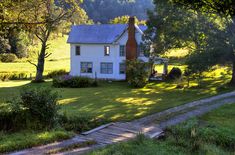 a white house sitting in the middle of a lush green field next to a forest