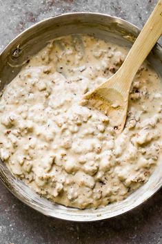 a wooden spoon is in a bowl filled with creamed meat and sauce on the table