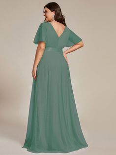 a woman in a long green dress is looking back at the camera and she has her hands on her hips