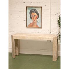 a painting hangs on the wall next to a bench in front of a brick wall