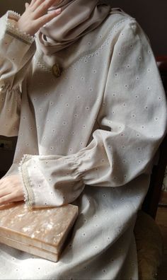 a woman wearing a hijab sitting down with her hands on her face and holding a book