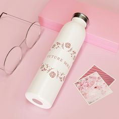 a white water bottle sitting on top of a pink table next to glasses and photos