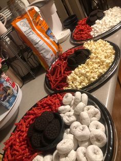 three trays filled with marshmallows, oreos and other snacks on a kitchen counter