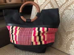 A beautiful purse to pair with your next outfit. It is a solid black base with wood handles and the middle part of the purse is pink/black and jute on a black base.  It is a hand held purse, which you can grasp by the round wooden handles at the top of the purse.  The dimensions of the purse are 14 inches in length, 13.5 in height. It can carry a lot of your valuables such as your phone, wallet, and even has room for more as shown in the first picture.  Price low for quick sale! Please allow 15- Traditional Black Shoulder Bag With Leather Handles, Black Handheld Shoulder Bag With Bamboo Handle, Traditional Black Handheld Bag, Black Rectangular Shoulder Bag With Bamboo Handle, Black Shoulder Bag With Bamboo Handle For Shopping, Black Bags With Bamboo Handle And Double Handle, Black Shoulder Bag With Bamboo Round Handle, Black Bags With Bamboo Double Handle, Black Bag With Bamboo Handle For Shopping