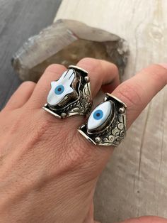 Unique statement evil eye rings. You can choose between the mother of pearl hamsa ring or the mother of pearl evil eye ring. Powerful rings that you can rock with your everyday outfits. In the pictures you can see the dimension of the rings. They are size adjustable what makes them the perfect gift for yourself and a love one. The smallest size recommended would be size 8, but you might be able to adjust a bit smaller than that, and can be open to bigger sizes. The bigger the size, the bigger th Symbolic Evil Eye Jewelry Ring, Symbolic Evil Eye Ring Jewelry, Spiritual Evil Eye Ring Jewelry, Handmade Symbolic White Rings, Symbolic Handmade White Rings, Spiritual Evil Eye Rings As Gift, Unique Silver Evil Eye Jewelry, Sterling Silver Evil Eye Ring, Silver Evil Eye Open Ring